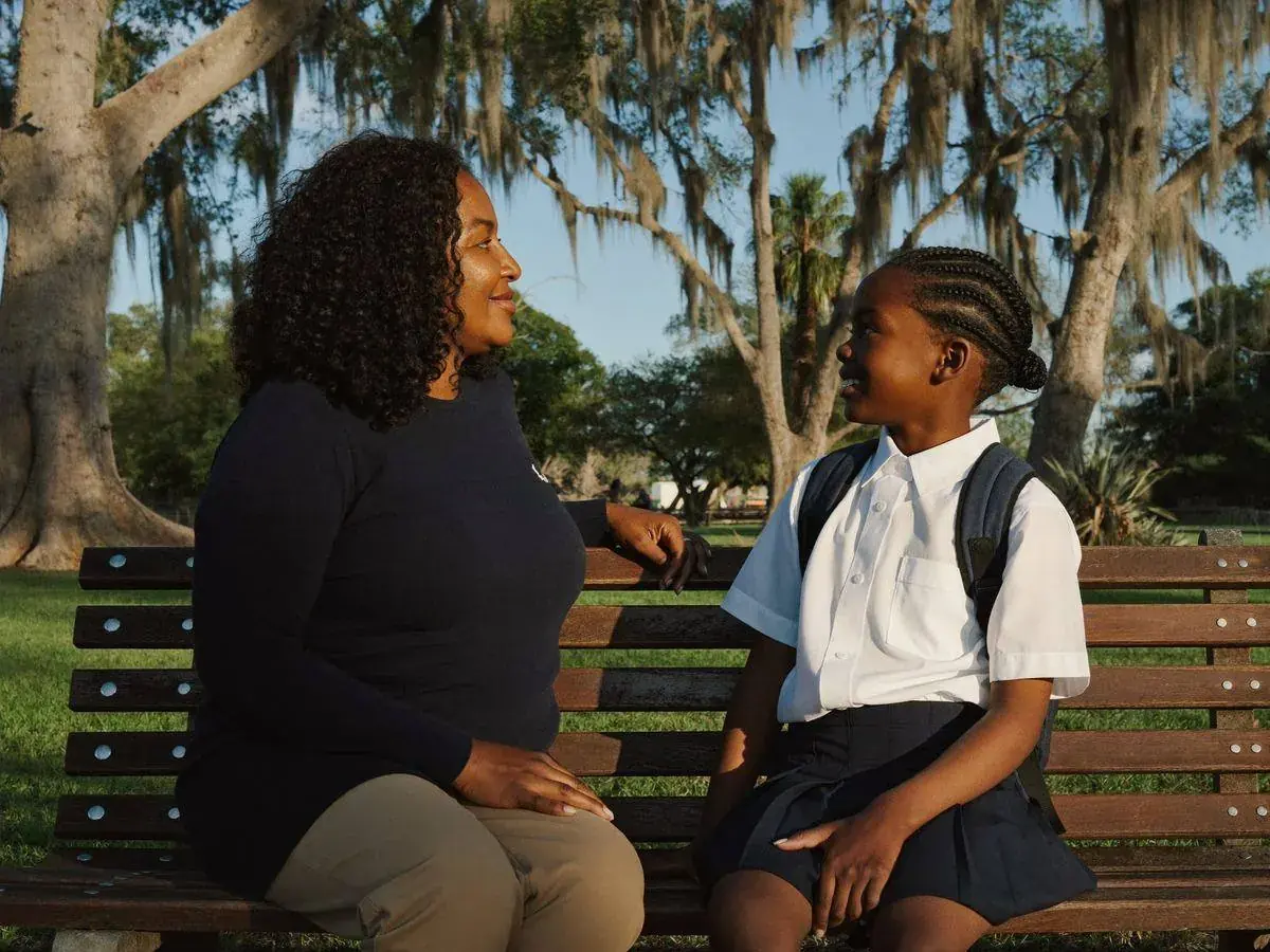 A mother and school-age child sharing a supportive moment on a park bench
